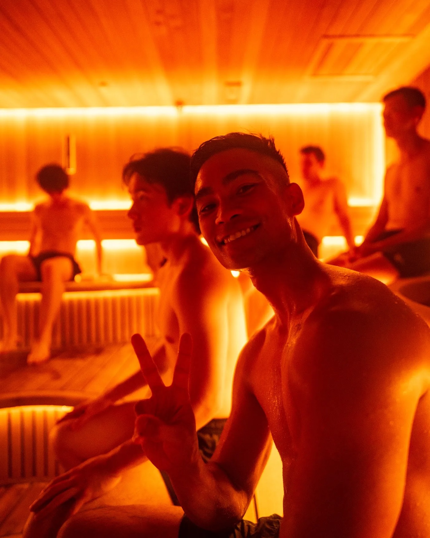 A member smiling with a peace sign in the red-lit sauna