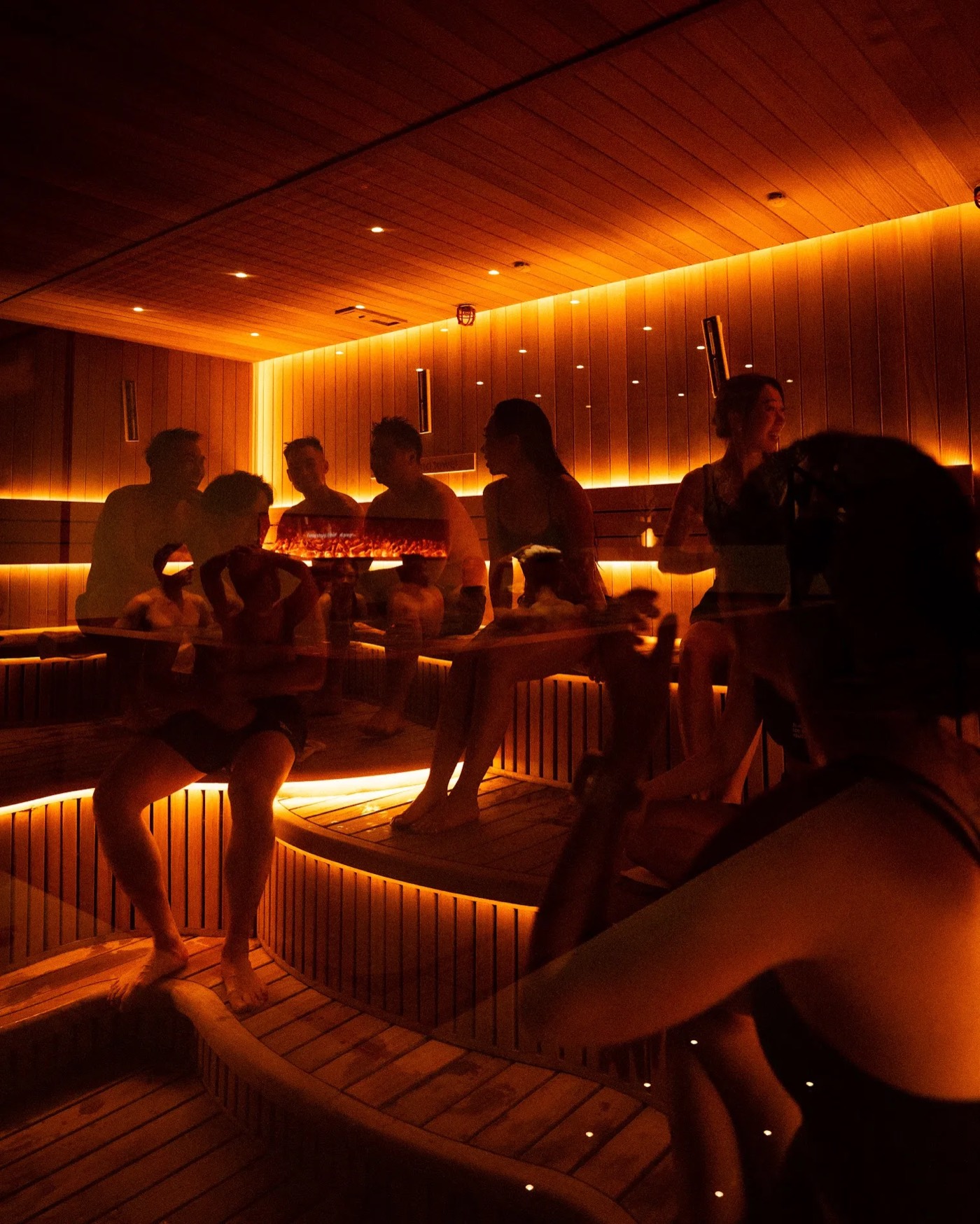 Friends talking across the benches of a warmly lit sauna