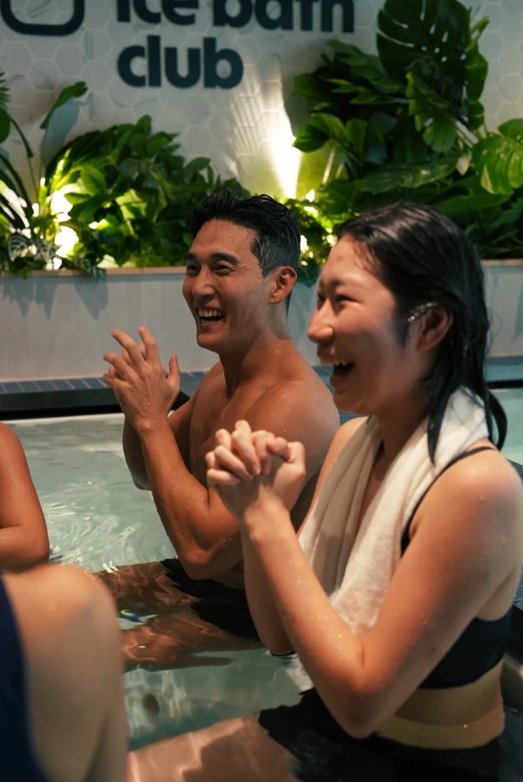 Two members laughing in the ice bath under the club sign